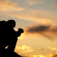 A silhouette of a man praying at sunset.